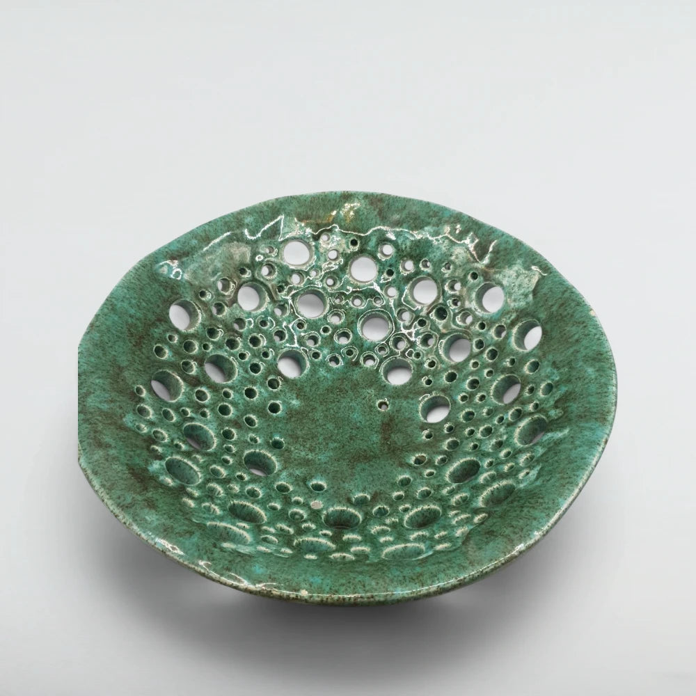 Pierced stoneware fruit bowl from above, showing verdigris glaze breaking around dozens of hand-cut holes