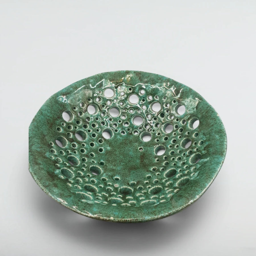 Pierced stoneware fruit bowl from above, showing verdigris glaze breaking around dozens of hand-cut holes
