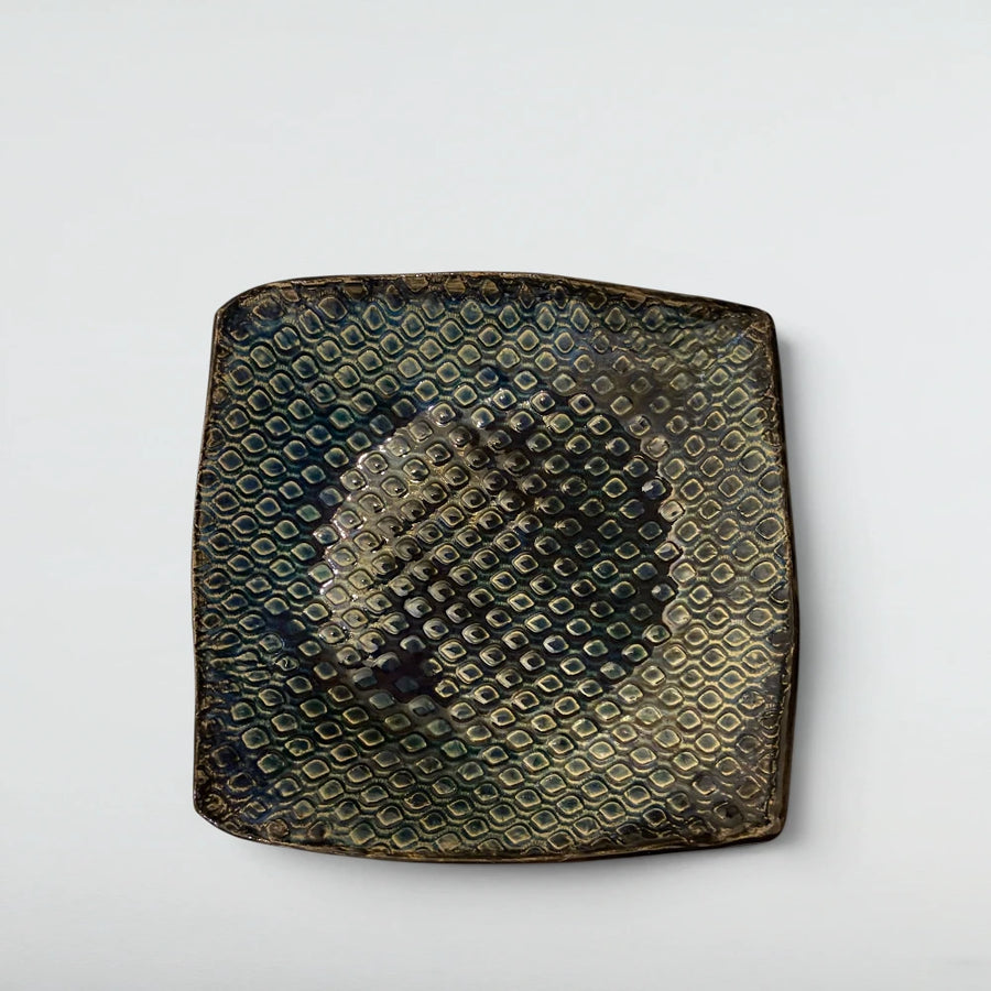 Square stoneware platter with raised dot grid flooded in teal and indigo glaze that shifts like feathers