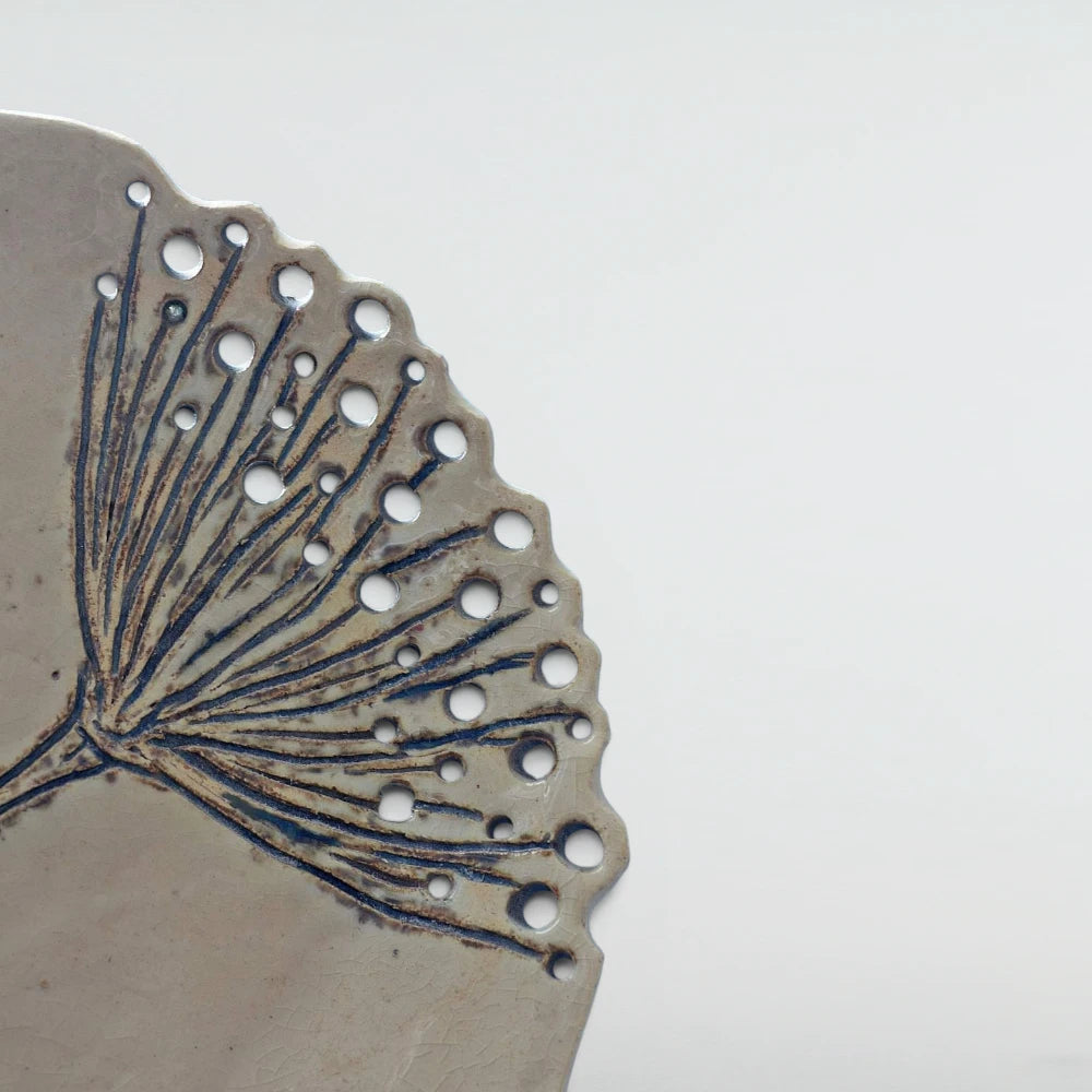 Detail of carved yarrow stems fanning into pierced holes along the scalloped edge of the crackle-glazed plate